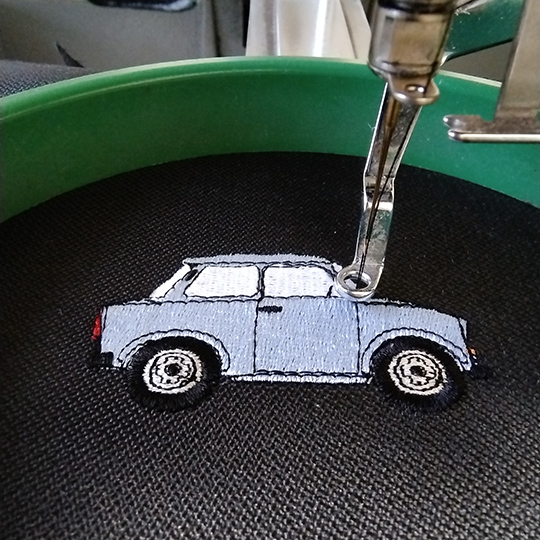 Gesticktes Trabant Auto auf schwarzem Stoff – Maschinenstickerei eines Oldtimers mit feinen Details